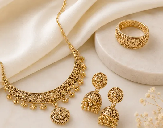 Gold-tone necklace, ring and jhumkas on a cream cloth
